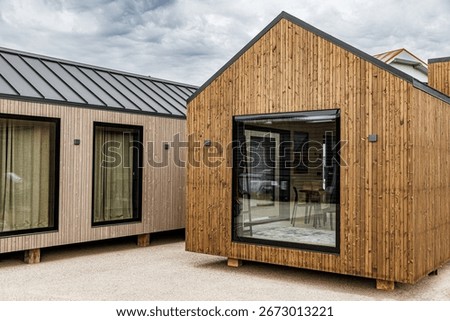 Compact prefab tiny house with timber cladding, large glass window, and minimalist Scandinavian-inspired design, offering eco-friendly and sustainable modern living solutions