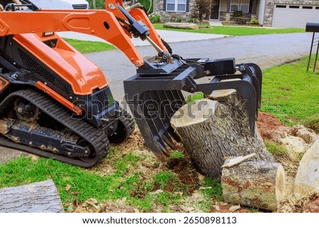 Compact skid steer track loader is working to remove large tree stump after strong tornado from quiet suburban area.