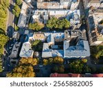 Compact urban area featuring light colored facades, sloped roofs, central courtyard with trees, bordered by streets and multi story buildings.