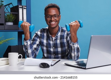 Company athletic businessman lifting weights while sitting at desk in office. Active and healthy young adult doing workout with fitness dumbbells in order to maintain body strong. - Powered by Shutterstock