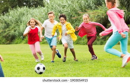 Company of children playing football on the playground in park