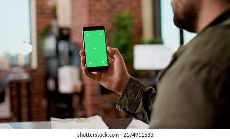 Company employee holding smartphone with greenscreen, using digital chroma key display with isolated mockup copyspace. Blank background on modern mobile phone, app technology in office. - Shutterstock ID 2174911533