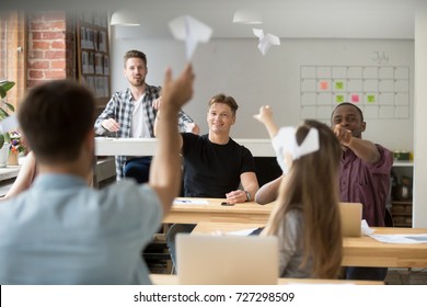 Company Employees Launching Paper Plane Towards Each Other. Colleagues Having Fun And Being Silly During Break From Workflow. Colleagues Entertaining Themselves At Workplace, Being Childish At Work. 