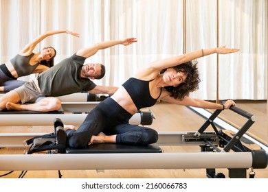 Company of fit sportspeople doing Mermaid exercise on pilates machines while stretching bodies during fitness training - Shutterstock ID 2160066783