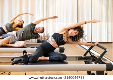 Company of fit sportspeople doing Mermaid exercise on pilates machines while stretching bodies during fitness training