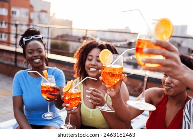 Company of four cheerful friends are enjoying tasty cocktails. Roof party. Interracial man and african women drink aperol with orange slices. Multiethnic group of people have fun and laugh together. - Powered by Shutterstock