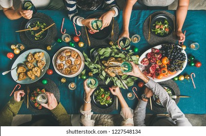 Company Of Friends Of Different Ages Gathering For Christmas Or New Year Party Dinner At Festive Table. Flat-lay Of Human Hands Holding Glasses With Drinks, Feasting And Celebrating Holiday, Top View