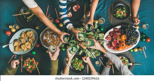 Company Of Friends Or Family Gathering For Christmas Or New Year Party Dinner At Festive Table. Flat-lay Of Human Hands Holding Glasses With Drinks, Feasting And Celebrating Holiday Together, Top View