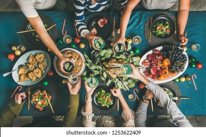 Company of friends gathering for Christmas or New Year party dinner at festive table. Flat-lay of human hands holding glasses with drinks, feasting and celebrating holiday together, top view - Shutterstock ID 1253622409