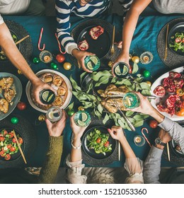 Company of friends gathering for Christmas or New Year party dinner at festive table. Flat-lay of hands holding glasses with drinks, feasting and celebrating holiday together, top view, square crop - Shutterstock ID 1521053360