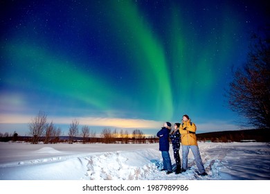 Company of friends tourist looks aurora northern lights night at forest, soft focus.