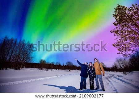 Company friends tourist looks aurora northern lights night at forest, soft focus.
