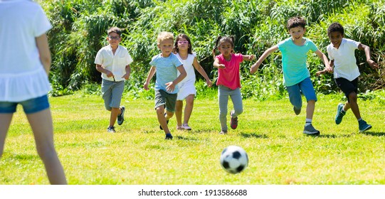 Company of glad children playing football on the playground in park. High quality photo