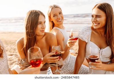 The company of gorgeous female friends having fun, cheers and drink wine, and enjoy picnic on the beach. Hen party. - Powered by Shutterstock