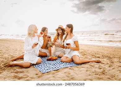 The company of gorgeous female friends having fun, cheers and drink wine, and enjoy picnic on the beach. Hen party. - Powered by Shutterstock