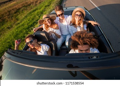Company of happy young girls and guys are sitting in a black convertible car road on a sunny day. Top view