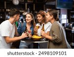 Company of joyful friends drinking beer, eating chips and talking with each other in the sport pub