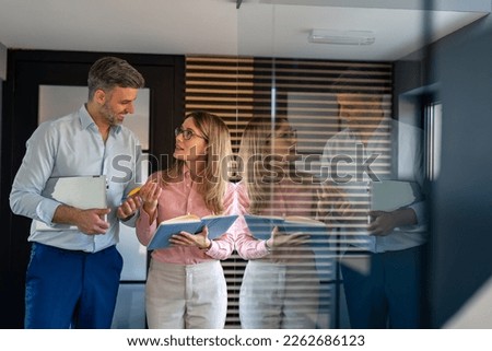 Company manager with his secretary going through business schedule. Business colleagues interacting with each other while walking in office corridor. Businessman and businesswoman working together.