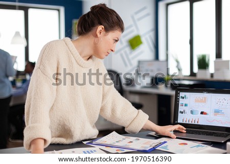 Company manager reading, analysing statistics on laptop in start up office. Executive entrepreneur, manager leader standing working on projects with diverse colleagues. Successful corporate