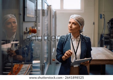 Company manager using touchpad while monitoring the processing machine in factory plant..