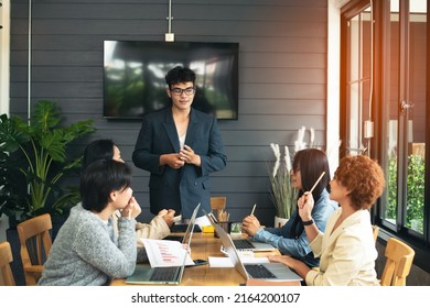 A Company Meeting By An Asian Young Man CEO, Presented To Colleagues Of The Business Successful At The Table In Small Room And Glass Window,  Congratulation At Job Done With Happy Emotional, Hand Up