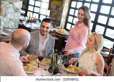 A Company Of People Dining In A Restaurant While Smiling Waitress Is Serving Them