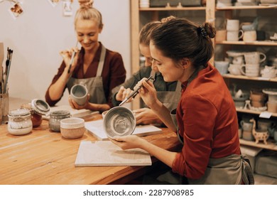 A company three cheerful young women friends are painting ceramics in pottery workshop  Have fun doing art 