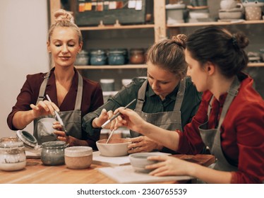 A company of three cheerful young women friends are painting ceramics in a pottery workshop. Lifestyle concept. - Powered by Shutterstock