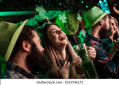The company of young people celebrate St. Patrick's Day. They have fun at the bar. They are dressed in carnival headgear.