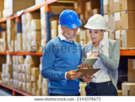Comparing notes for accuracy. Shot of two people doing an inventory check in a warehouse.