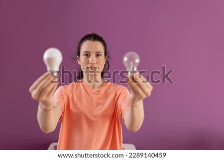 Comparison economic and normal light bulb.
Eco living and sustainability concept. Smiling woman comparing energy saving light bulb with incandescent lamp 