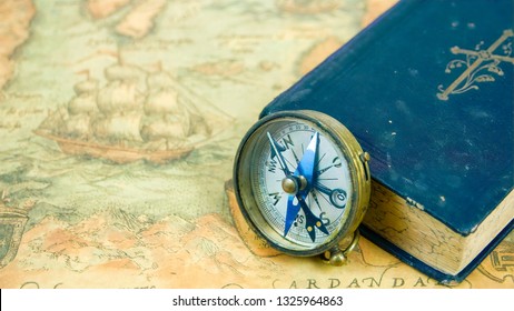 The compass beside a blue book with a cross on the cover. The compass and the book is on top of a navigational map - Shutterstock ID 1325964863