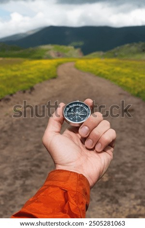 Compass in hand against the background of a mountain road, vertical photo. Choosing a path in travel and hiking