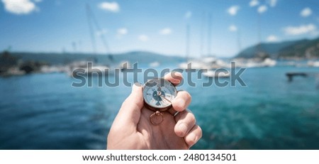 Compass in hand on the background of yachts and the sea. Background on the theme of travel, navigation, voyage, hike, etc. Shallow depth of field, sharpness on the compass.