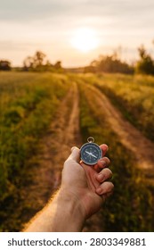 A compass held in a hand against the backdrop of a country road at sunset