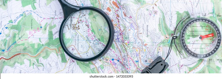 A compass, a map and a loupe on a table. Detail topographic map. Magnifier. Get directions on the map. Terrain orientation. Scouting. Scout equipment for orientation. Orienteering. Header.  Banner.