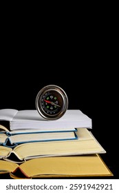 A compass is on top of a stack of books. The books are open and the compass is on top of the open book