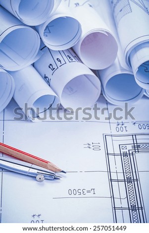 compass pencil and big stack of white rolled up blueprints 