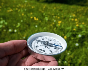 A compass in person's hand in park with flowers. Orient yourself in current situation (urban conditions). Follow innner compass, intuition concept, public sentiments