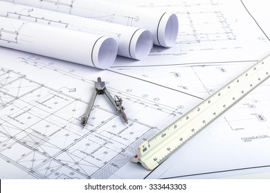 Compasses and Architect scale ruler placed on the desk, filled with building plans. In order to work in a building