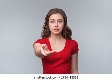 Compassionate Young Brunette Woman Isolated On Gray Background Offers For Help, Reaching Hand Of Hand To The Camera