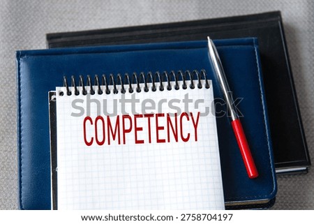 COMPETENCY - word in a notebook against the background of books lying on a gray background.