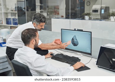 Competent male workers examining 3d model of face mask on computer while browsing computer in modern light office during coronavirus epidemic - Powered by Shutterstock