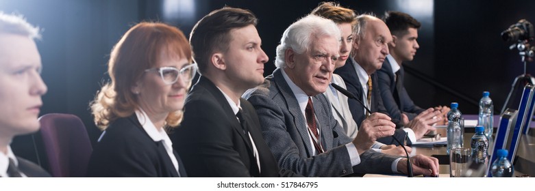 Competition between politician during political debate before election. Older confident man in suit speaking to microphone - Shutterstock ID 517846795