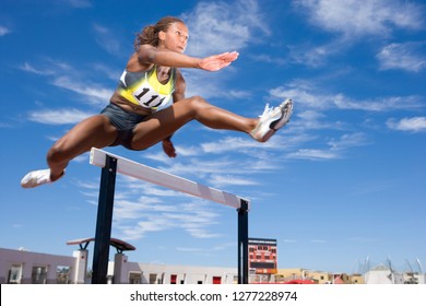 Competitive female athlete jumping hurdle in race on running track