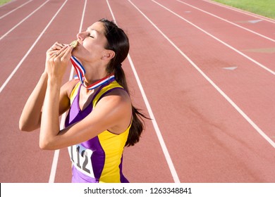 Competitive female athlete kissing gold medal on race track - Powered by Shutterstock