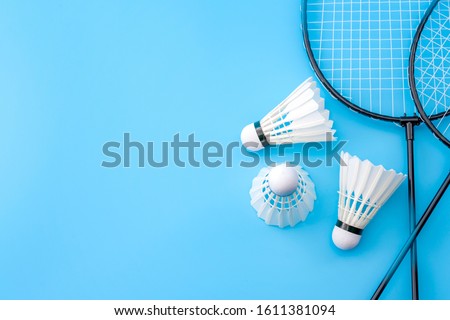 Competitive sports and high performance in tournament match conceptual idea with badminton rackets and shuttlecock (birdie) isolated on blue court background with copy space