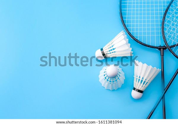 Competitive sports and\
high performance in tournament match conceptual idea with badminton\
rackets and shuttlecock (birdie) isolated on blue court background\
with copy space