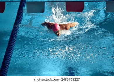 Competitive swimmer, wearing pink swim cap and goggles, powers through water with butterfly stroke, creating dynamic splash in blue swimming pool lane. Concept of aquatic sport, energy. - Powered by Shutterstock