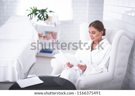 Complete relaxation. Lovely young woman reading booklet at cosmetologist cabinet